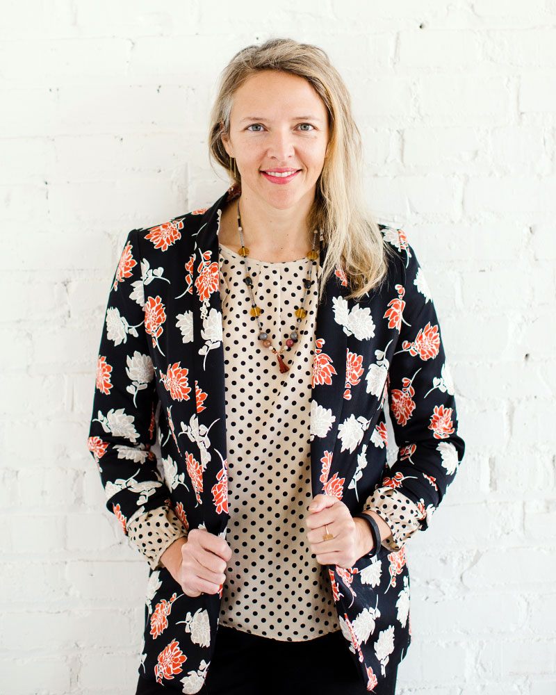 woman in colorful jacket standing against white brick wall