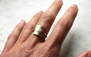 Hand wearing a ring with text Be Brave stamped into it