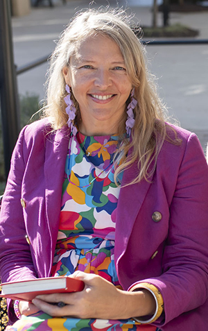 Jolinda Anderson, owner of Shapes & Colors and lead web designer sits outside on a sunny day holding a notebook